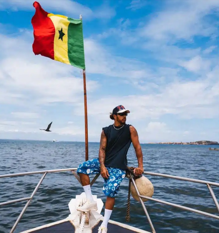 Emu par sa visite à la maison des esclaves sur l'île de Gorée, Lewis Hamilton pose dos à la mer et au drapeau du Sénégal 